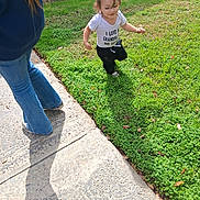 Ezra is registered to the contest to win money with this photo: child, toddler, outdoor, garden, grass, sidewalk, adult, walking, smiling, blonde_hair, white_shirt, black_pants, shoes, sunlight, shadow, plants, greenery, park, portrait, family