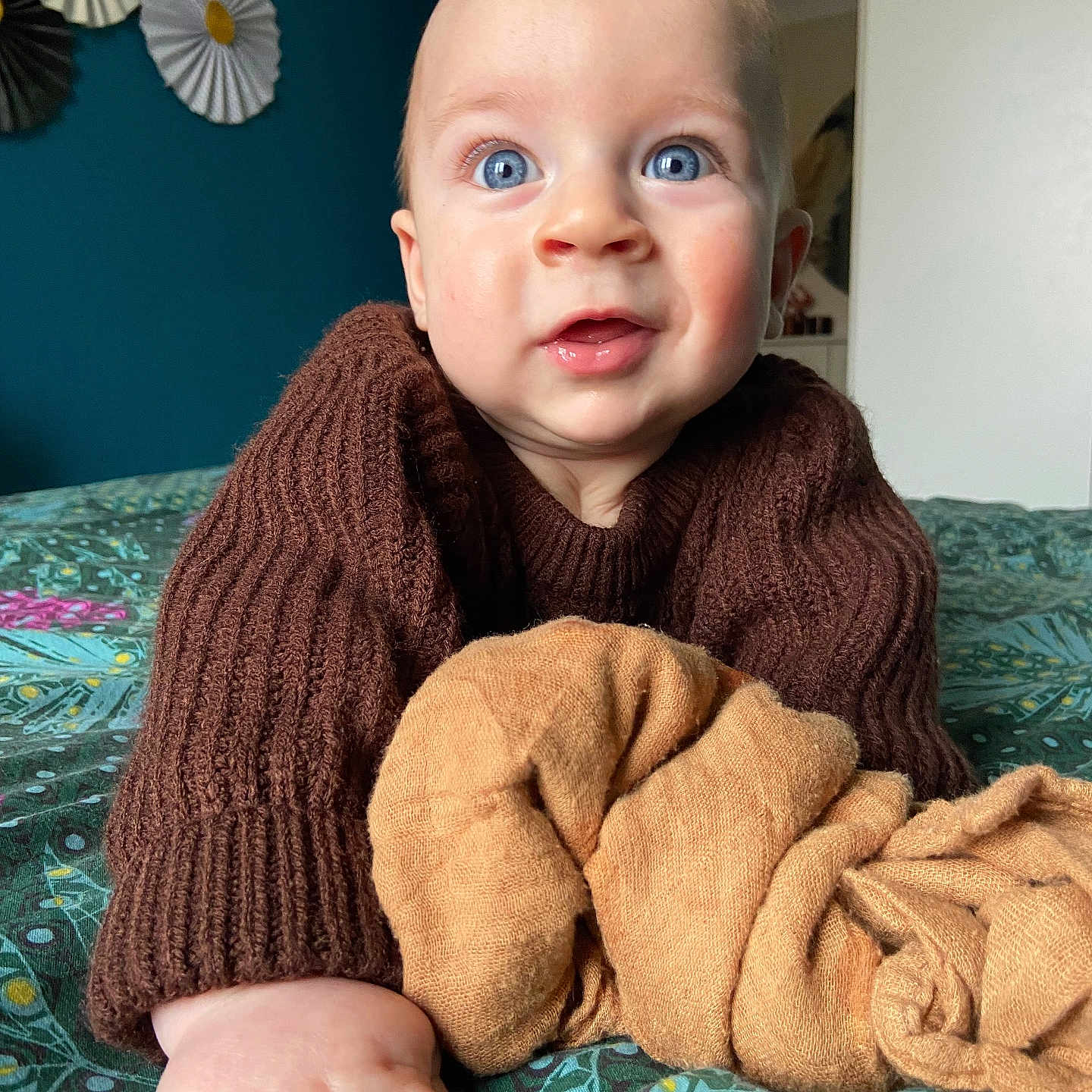 Eden participe au concours pour gagner de l'argent avec cette photo : baby, bedspread, blanket, blue_eyes, brown_sweater, child, cozy, curious_expression, decor, face, hand, home, indoor, lying_down, pattern, person, portrait, skin, soft_texture, young_child