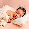 baby, sleeping, crown, plush_toy, lamb, pillow, lace_skirt, soft_texture, peach_background, infant, cute, resting, adorable, child, portrait, peaceful, newborn, soft_lighting, cozy, indoor