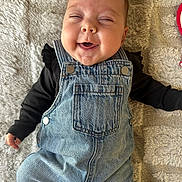 Lynaïa a rejoint le concours — aidez-le/la à gagner de superbes lots ! baby, infant, denim_overalls, black_shirt, smiling, happy, face, cheeks, lying_down, blanket, texture, clothing, cute, child, portrait, indoors, one_person, casual, joyful, small_hand
