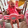 baby, pink_dress, swing, indoor, child, smiling, happy, toy, furniture, floor, nursery, plastic, seat, person, legs, hands, head, face, wood_floor, home