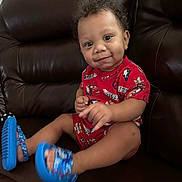 Josiah joined the competition — help win amazing prizes! toddler, child, curly_hair, red_clothing, blue_sandals, smile, face, sitting, leather_couch, indoor, cute, happy, young_child, portrait, person, feet, legs, furniture, home, casual_clothing