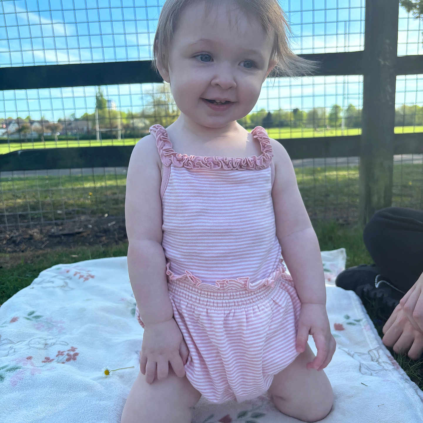 Ivey-Leigh is registered to the contest to win money with this photo: blanket, casual, child, daylight, expression, face, fence, field, grass, hair, happy, kneeling, nature, outdoor, person, pink_clothing, romper, smiling, sunlight, toddler
