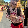 Nevaeh is registered to the contest to win money with this photo: child, girl, smiling, outdoor, sunlight, backpack, toy, sweater, red_skirt, people, group, fence, sidewalk, trees, daylight, happy, portrait, casual_clothing, playground, school