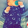 baby, infant, pacifier, onesie, sleepwear, bed, pillow, blanket, blue, pattern, football_helmet, star, hand, face, mouth, sleeping, resting, indoors, child, cute
