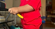 Joseph is registered to the contest to win money with this photo: child, smiling, red_shirt, black_pants, toy, indoor, person, face, pants, sleeve, hand, holding, furniture, carpet, living_room, television, basket, blurred_background, hair, standing