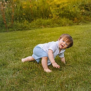 Marcus is registered to the contest to win money with this photo: baby, child, toddler, crawling, outdoor, garden, grass, lawn, portrait, face, blue_eyes, brown_hair, smiling, white_shirt, striped_shorts, barefoot, nature, flowers, daylight, photography