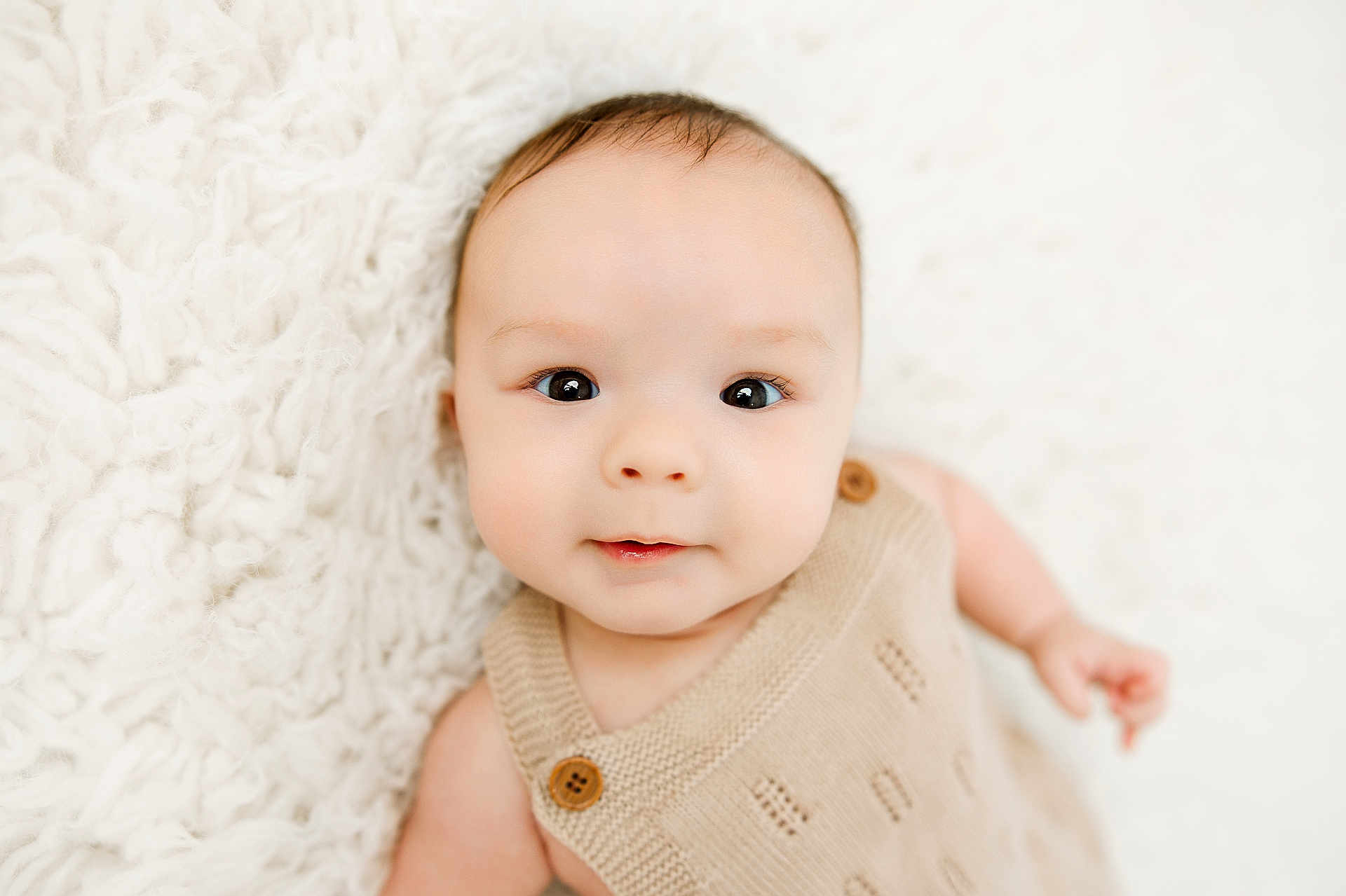 Bryson is registered to the contest to win money with this photo: baby, infant, face, eyes, smile, knitted_outfit, beige_clothing, wooden_buttons, blanket, white_background, soft_texture, cute, child, portrait, lying_down, skin, head, closeup, newborn, adorable