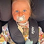 toddler, child, pacifier, car_seat, hair_tie, blanket, blue_eyes, safety_harness, clothing, indoors, seat, person, baby, cute, young_child, infant, patterned_shirt, car_interior, soft_toy, portrait