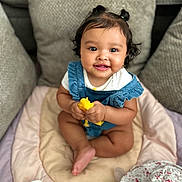 Mariana is registered to the contest to win money with this photo: baby, child, infant, pigtails, smiling, sitting, toy, pillow, cushion, blanket, clothing, face, headwear, baby_products, indoor, cute, happy, person, skin, photography