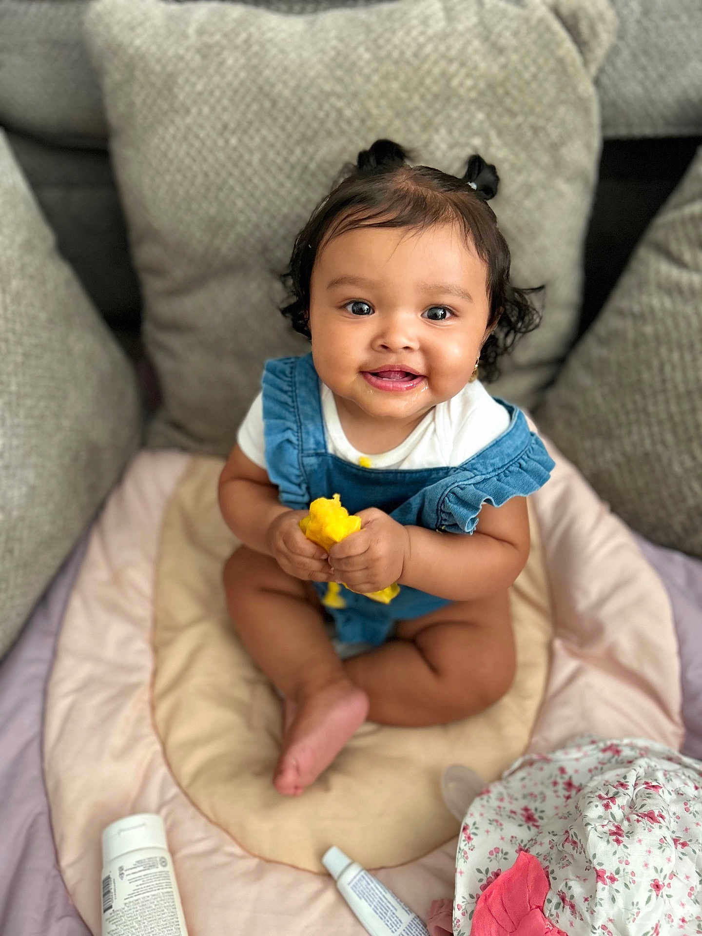 Mariana is registered to the contest to win money with this photo: baby, child, infant, pigtails, smiling, sitting, toy, pillow, cushion, blanket, clothing, face, headwear, baby_products, indoor, cute, happy, person, skin, photography