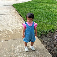 Natalia is registered to the contest to win money with this photo: toddler, child, sidewalk, grass, outdoor, greenery, building, stairs, footwear, clothing, shorts, person, curly_hair, daylight, casual, pink, blue, shoes, nature, concrete