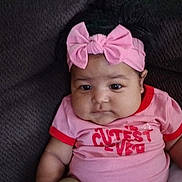 Aurora is registered to the contest to win money with this photo: baby, infant, pink_headband, bow, pink_outfit, sitting, couch, chubby_cheeks, cute, child, indoors, portrait, clothing, footwear, relaxed, person, young_child, headwear, expressionless, comfortable