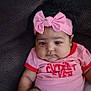 baby, infant, pink_headband, bow, pink_outfit, sitting, couch, chubby_cheeks, cute, child, indoors, portrait, clothing, footwear, relaxed, person, young_child, headwear, expressionless, comfortable