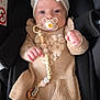 baby, bow, pacifier, car_seat, knitted_dress, beige, patterned_tights, pacifier_clip, name_beads, infant, child, cute, portrait, indoors, seat_belt, clothing, hands, headwear, face, person