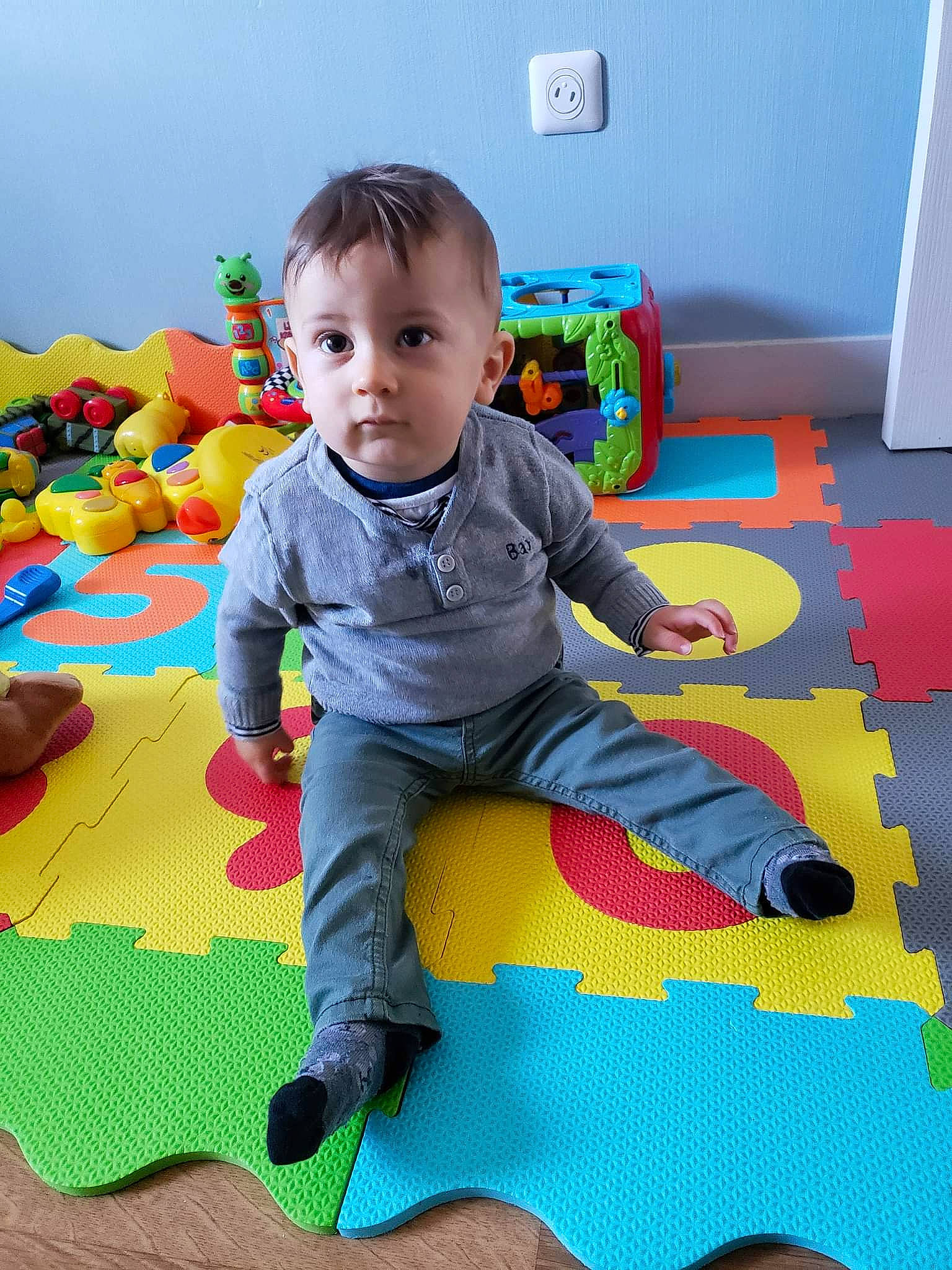 Elio a rejoint le concours — aidez-le/la à gagner de superbes lots ! baby, baby_playing_with_toys, baby_products, baby_toddler_clothing, baby_toys, carpet, child, comfort, floor, flooring, fun, pattern, person, play, playmat, product, room, sitting, sock, toddler
