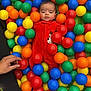 Thiago is registered to the contest to win money with this photo: baby, child, red_onesie, ball_pit, colorful_balls, plastic_balls, reindeer_patch, hand, phone, playful, indoor, curious, portrait, person, smile, multicolor, toy, fun, cute, infant