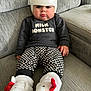 baby, child, helmet, couch, gray_couch, sweatshirt, milk_monster, checkered_pants, chicken_slippers, footwear, plush_slippers, indoor, seated, cute, face, person, clothing, infant, comfort, home
