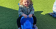 Ayla joined the competition — help win amazing prizes! black_pants, blue_toy, casual_clothing, checkered_shoes, child, daytime, denim_jacket, fun, green_grass, happy, kid, outdoor, playground, playing, pony_tail, recreation, rocking_toy, shadow, smiling, sunlight