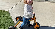Ayla joined the competition — help win amazing prizes! toddler, tricycle, playground, outdoor, child, smiling, grass, concrete, sunny, toy, play_equipment, casual_clothing, jeans, sneakers, play, daytime, park, happy, person, recreation