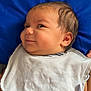 Colson joined the competition — help win amazing prizes! baby, infant, child, smiling, cheeky, striped_clothing, white_bib, blue_pillow, lying_down, face, head, skin, hair, cute, indoors, portrait, expression, young_child, person, closeup