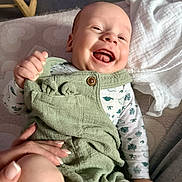 Liam participe au concours pour gagner de l'argent avec cette photo : baby, smiling, infant, green_overalls, white_blanket, hand, happy, clothing, lying_down, cute, child, indoors, soft_surface, portrait, skin, face, joy, expression, person, newborn