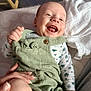 baby, smiling, infant, green_overalls, white_blanket, hand, happy, clothing, lying_down, cute, child, indoors, soft_surface, portrait, skin, face, joy, expression, person, newborn