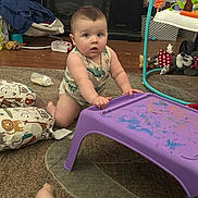 Andrew joined the competition — help win amazing prizes! baby, child, indoor, carpet, table, toy, bottle, cushion, floor, person, onesie, paint, purple_table, wooden_floor, furniture, curious, kneeled, messy_room, playtime, dinosaur_print