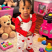 Lynn Hayley is registered to the contest to win money with this photo: child, toddler, girl, curly_hair, white_bows, red_shoes, heart_overalls, stuffed_teddy, pink_toy_car, stacking_rings, playroom, rug, wood_floor, toy_piano, portrait, big_eyes, cute, smile, standing, indoor