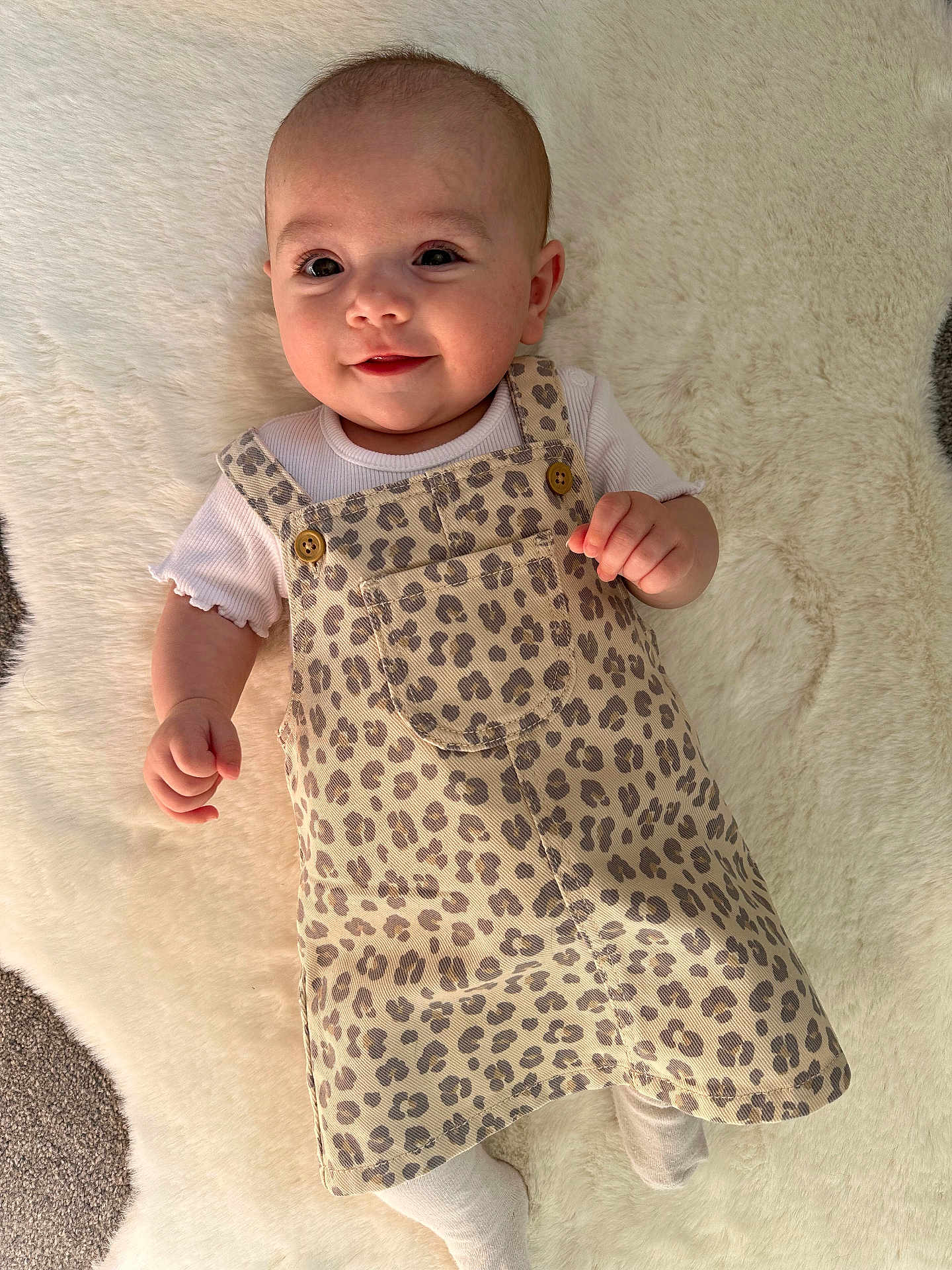 Hallie joined the competition — help win amazing prizes! baby, infant, smiling, face, leopard_print, dress, white_shirt, buttons, soft_rug, lying_down, cute, child, apparel, happy, skin, head, eyes, hand, footwear, indoors