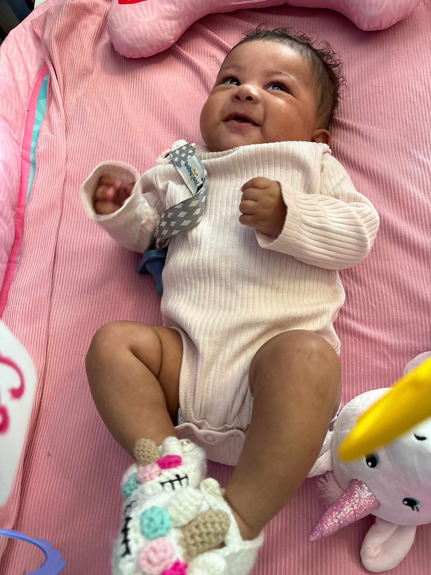 Delani joined the competition — help win amazing prizes! baby, infant, smiling, lying_down, pink_blanket, onesie, unicorn_slippers, plush_toy, soft_toys, indoors, cute, child, happy, cozy, small_hands, small_feet, looking_up, infant_clothing, baby_accessories, play_area