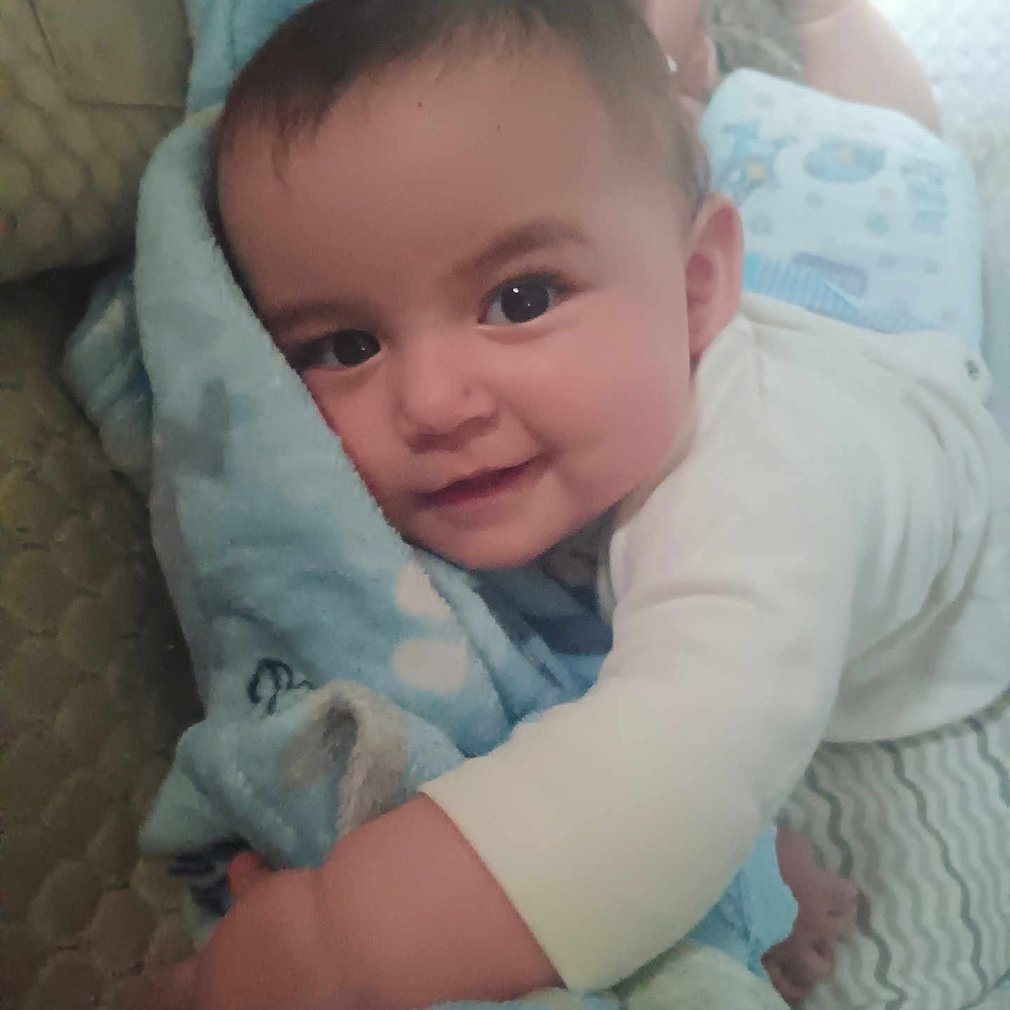 Ruthanne is registered to the contest to win money with this photo: baby, blanket, blue_blanket, child, closeup, cute, eyes, face, hand, happy, head, indoors, infant, lying_down, patterned_surface, skin, smiling, soft_texture, toddler, white_clothing