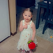 Cambria is registered to the contest to win money with this photo: child, girl, dress, white_dress, braided_hair, smiling, red_bucket, indoor, kitchen, floor_tiles, dining_table, chairs, carpet, toy, happy, cute, portrait, young_child, love_text, black_heart_emoji