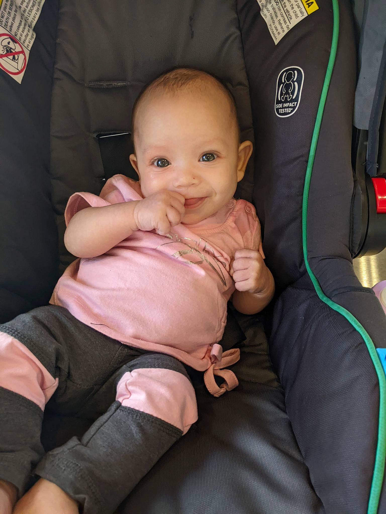 Arya is registered to the contest to win money with this photo: arm, baby, baby_carriage, baby_toddler_clothing, car_seat, cheek, comfort, finger, gesture, hand, joy, lap, leg, person, pink, seat_belt, skin, smile, textile, thigh