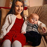 Giuliana participe au concours pour gagner de l'argent avec cette photo : child, baby, sibling, couch, pillow, red_dress, white_cardigan, baby_vest, indoor, smile, serious_expression, holding_hands, family, happy, portrait, home, cozy, holiday, cute, kids