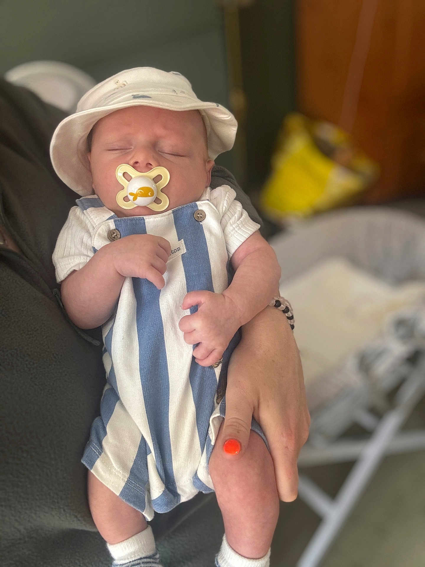 Austin is registered to the contest to win money with this photo: baby, sleeping, pacifier, hat, striped_clothing, hand, adult, nail_polish, orange_nail_polish, romper, infant, closeup, indoor, person, holding, cute, newborn, soft_lighting, peaceful, portrait