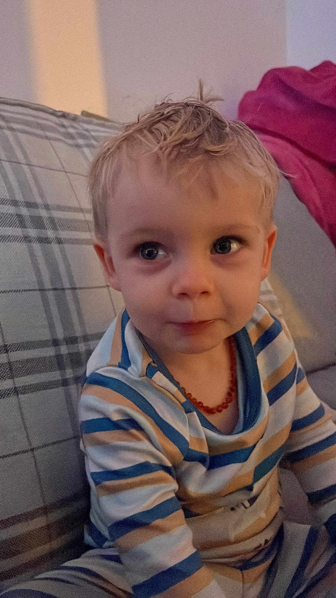 Elliot joined the competition — help win amazing prizes! toddler, child, pajamas, blonde_hair, striped_clothing, necklace, plaid_couch, indoor, portrait, sitting, curious, face, young_child, cozy, home, person, cute, casual, young, infant