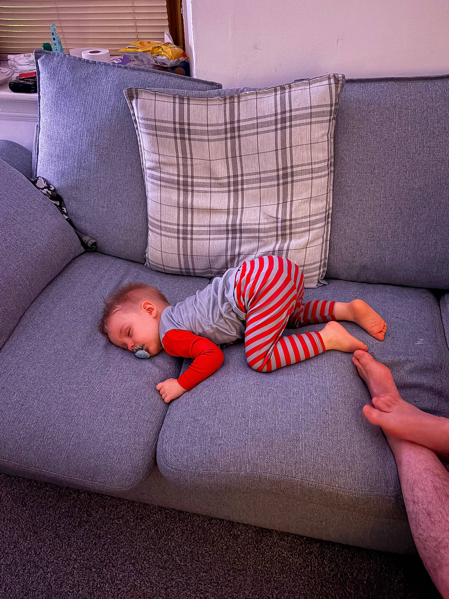 Elliot is registered to the contest to win money with this photo: adult, carpet, casual, child, couch, cozy, feet, furniture, gray_couch, home, indoor, pacifier, pajamas, peaceful, plaid_pillow, relaxation, resting, sleeping, striped_clothing, toddler