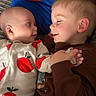 baby, toddler, siblings, children, portrait, close_up, smiling, lying_down, affection, interaction, face, eyes, hands, apple_print, clothing, brown_shirt, blue_background, couch, indoors, family