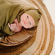 Jace is registered to the contest to win money with this photo: baby, infant, blanket, hat, basket, rug, knitwear, child, portrait, cozy, soft_lighting, smile, cute, newborn, indoor, warm_colors, texture, resting, wrapped, peaceful