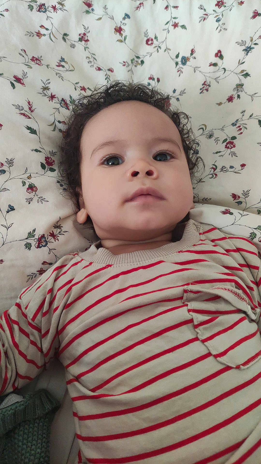 Louis Joseph a rejoint le concours — aidez-le/la à gagner de superbes lots ! baby, blue_eyes, calm_expression, child, close_up, clothing, curly_hair, cute, face, floral_blanket, indoors, infant, lying_down, person, pocket, portrait, skin, soft_light, striped_shirt, young_child