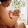 baby, woman, glasses, dress, holding, indoor, natural_light, plant, headband, bow, closeup, portrait, skin, face, arm, love, tenderness, child, seated, cozy