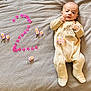 baby, infant, blanket, number_two, pink_flowers, onesie, cute, milestone, lying_down, soft_texture, celebration, newborn, portrait, face, hands, feet, cozy, expression, baby_clothes, baby_boy