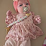 adorable, baby, beaded_pacifier_clip, bow, changing_pad, close_up, dress, fabric, floral_pattern, hands, headband, indoor, infant, leggings, newborn, pacifier, pink_clothing, portrait, soft_texture, toy