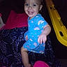 baby, blanket, blue_outfit, child, dark_background, face, family_photo, flash_photography, happy, indoor, infant, low_light, patterned_blanket, play_structure, portrait, rainbow_pattern, sitting, smiling, toy, yellow