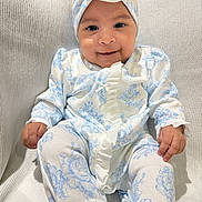 Husna is registered to the contest to win money with this photo: baby, blue_flower_pattern, child, comfortable, cushion, cute, flower, hands, happy, headband, indoors, infant, legs, portrait, sitting, smile, soft, texture, white_clothing, young_child