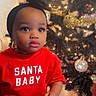 bow, celebration, child, christmas, christmas_tree, cute, decorations, festive_clothing, headband, holiday, holiday_season, indoors, lights, ornaments, portrait, red_shirt, smiling, striped_pants, toddler, young_child