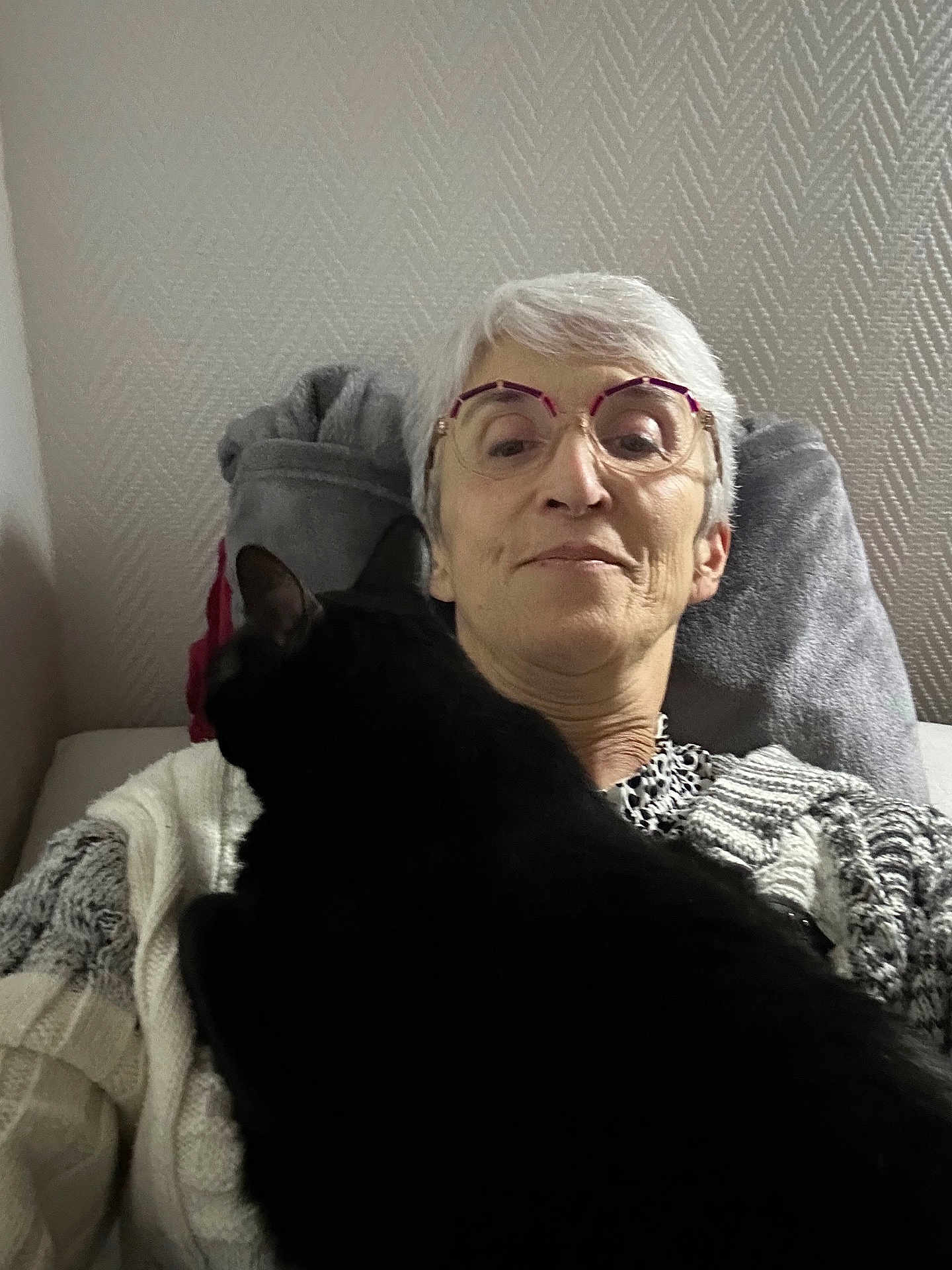 Solange Fournou a rejoint le concours — aidez-le/la à gagner de superbes lots ! animal, black_cat, casual, cat, closeup, comfort, couch, cozy, glasses, home, indoor, knitted, older_adult, pet, pillow, portrait, relaxing, resting, sweater, woman