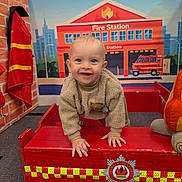 Jaxson joined the competition — help win amazing prizes! toddler, child, smiling, toy, fire_truck, fire_station, indoor, play, red, beige, sweater, carpet, firefighter_jacket, background, happy, climbing, wooden, cute, decor, person