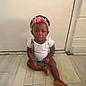 toddler, child, baby, indoor, floor, headband, white_shirt, shorts, sitting, wooden_floor, door, curious, calm, young_child, portrait, casual_clothing, barefoot, black_hair, pink_accessory, home